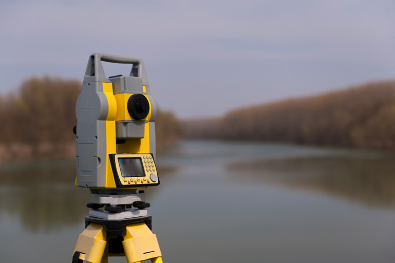 Yellow total station by river in overcast weather