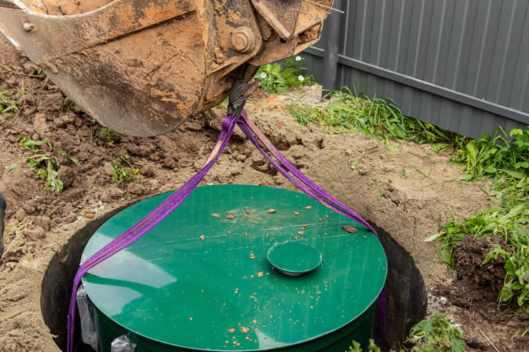 Excavator lifting septic tank with straps